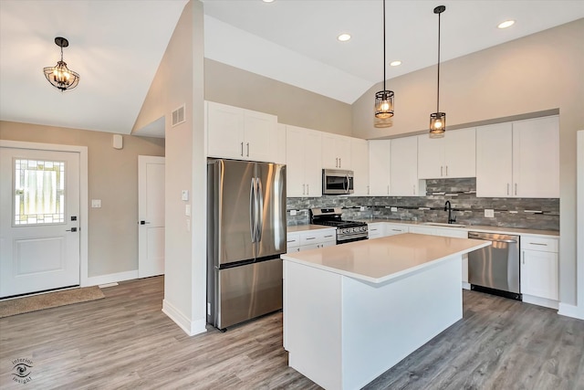 kitchen featuring a center island, decorative light fixtures, light wood-type flooring, white cabinetry, and appliances with stainless steel finishes