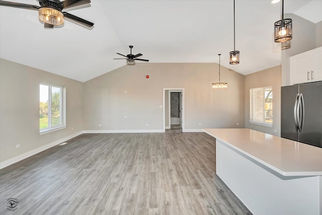 kitchen with lofted ceiling, hanging light fixtures, stainless steel fridge, light wood-type flooring, and white cabinets