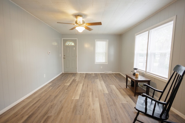 interior space featuring wooden walls, light hardwood / wood-style floors, ornamental molding, and ceiling fan