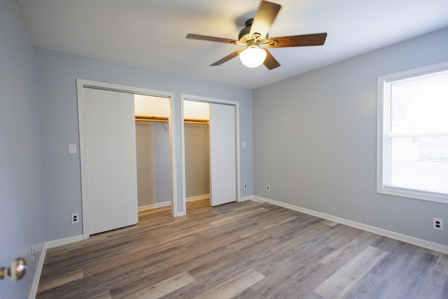 unfurnished bedroom with wood-type flooring, two closets, and ceiling fan