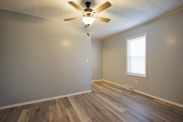 empty room featuring wood walls, ceiling fan, hardwood / wood-style floors, and crown molding