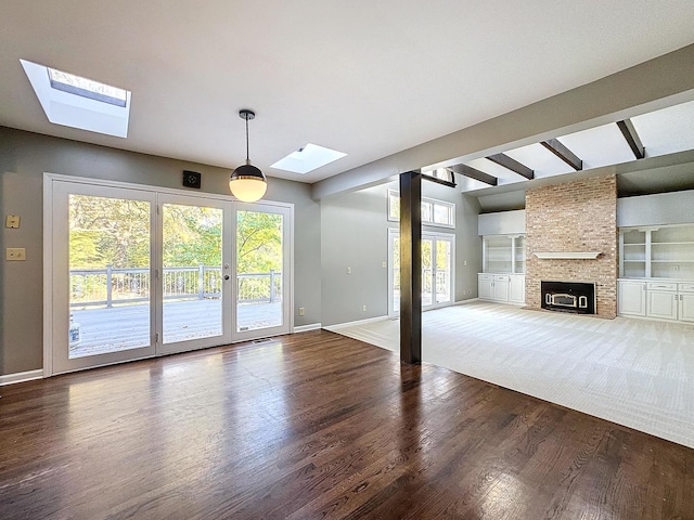 unfurnished living room with hardwood / wood-style flooring, beamed ceiling, a brick fireplace, and plenty of natural light