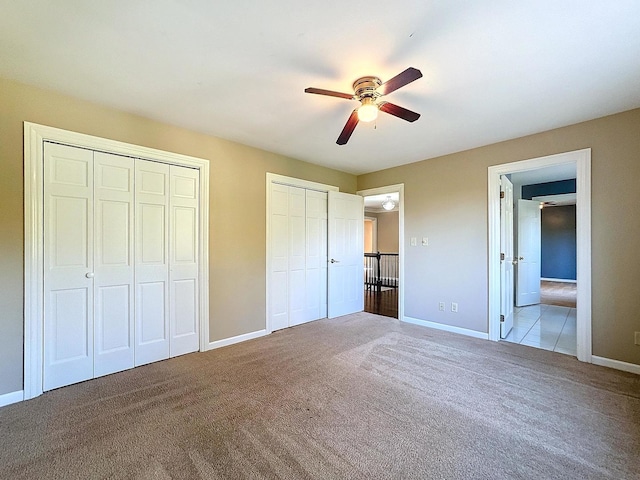 unfurnished bedroom with ceiling fan, multiple closets, and light colored carpet