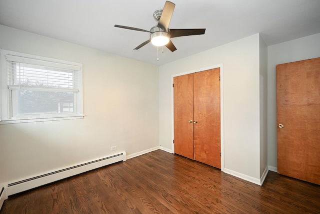 unfurnished bedroom featuring a baseboard heating unit, a closet, baseboards, and wood finished floors