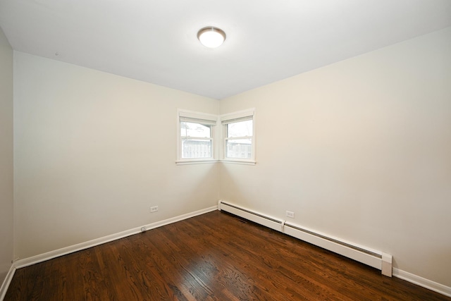 spare room with a baseboard heating unit, dark wood finished floors, and baseboards