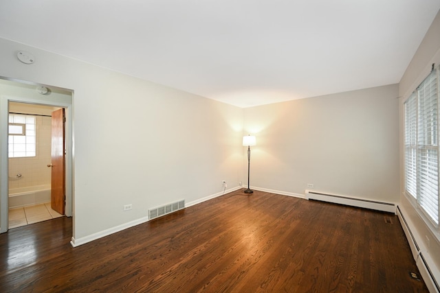 spare room featuring a baseboard radiator, wood finished floors, visible vents, and baseboards