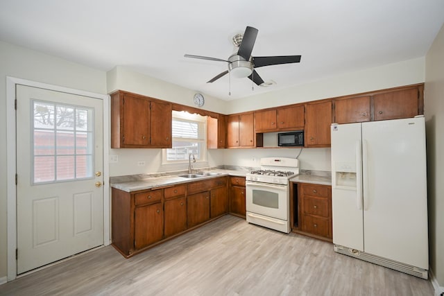 kitchen with white appliances, light wood-style floors, brown cabinetry, and a sink