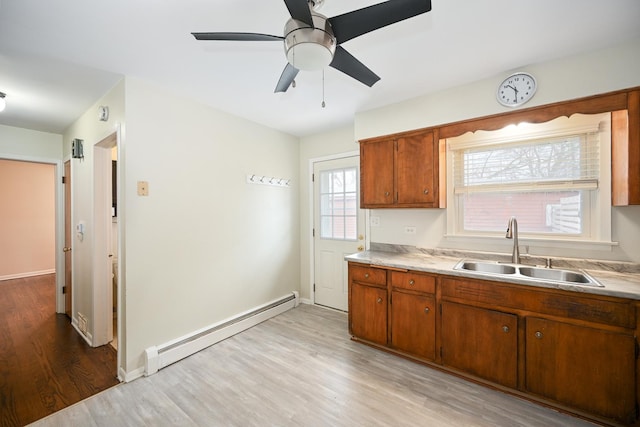 kitchen with a baseboard radiator, light countertops, a sink, and light wood finished floors