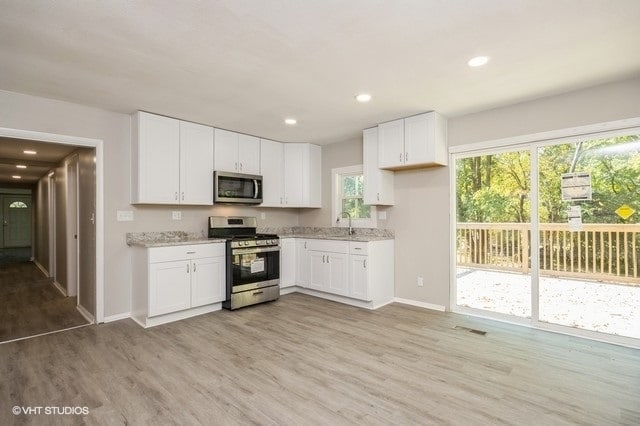 kitchen with appliances with stainless steel finishes, light hardwood / wood-style floors, white cabinetry, and light stone countertops