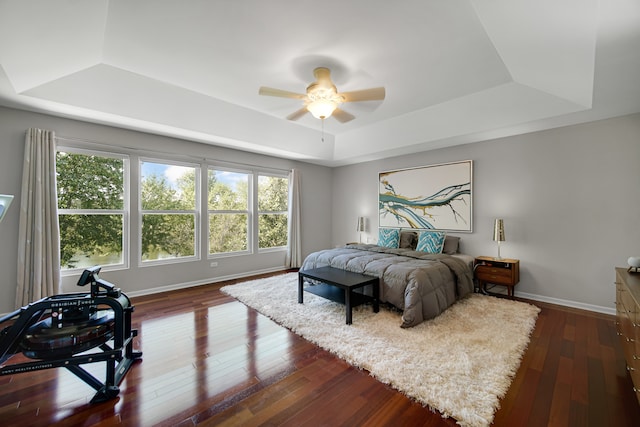 bedroom featuring a raised ceiling, dark wood-type flooring, and ceiling fan