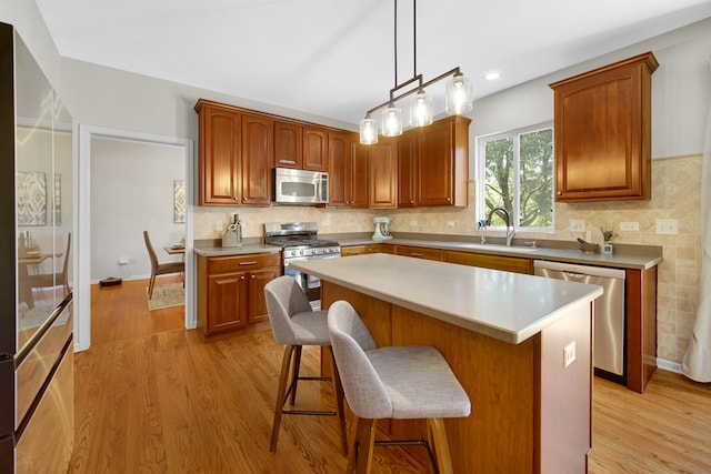 kitchen featuring appliances with stainless steel finishes, decorative backsplash, light wood-type flooring, a center island, and sink