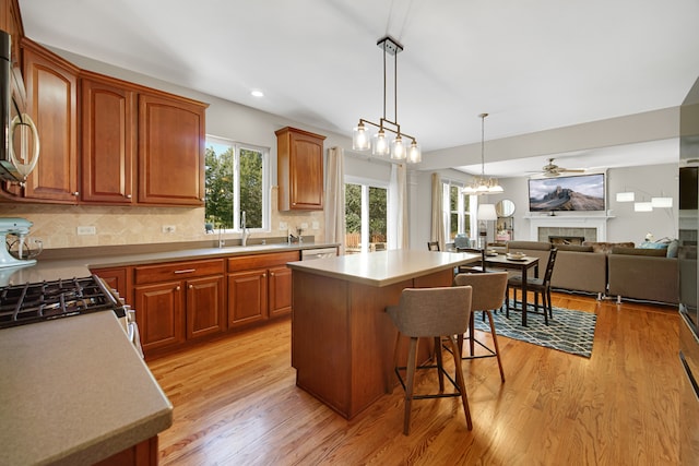 kitchen with decorative backsplash, light hardwood / wood-style floors, a fireplace, a center island, and ceiling fan