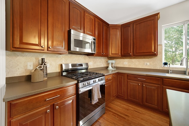 kitchen with appliances with stainless steel finishes, backsplash, sink, and light hardwood / wood-style flooring