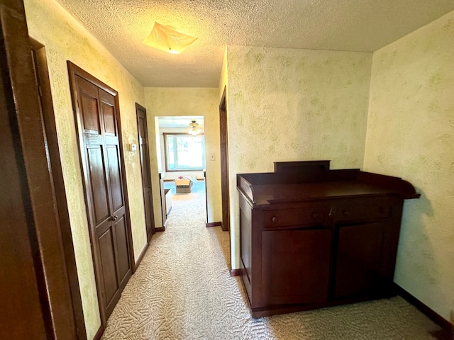 corridor with a textured ceiling and light colored carpet