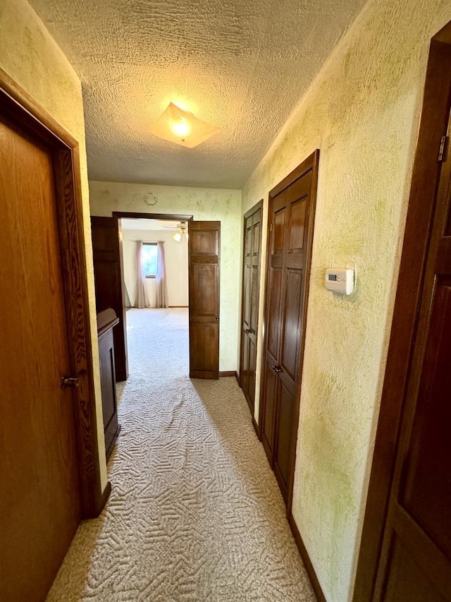 hallway with baseboards, a textured ceiling, a textured wall, and light carpet