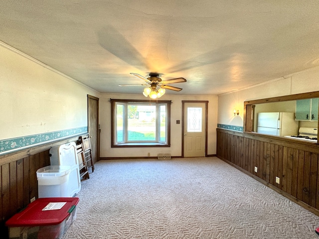 interior space with light carpet, wooden walls, ceiling fan, and a textured ceiling