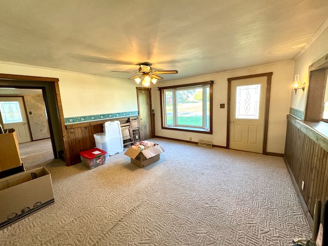 interior space featuring a textured ceiling, wood walls, light carpet, ornamental molding, and ceiling fan