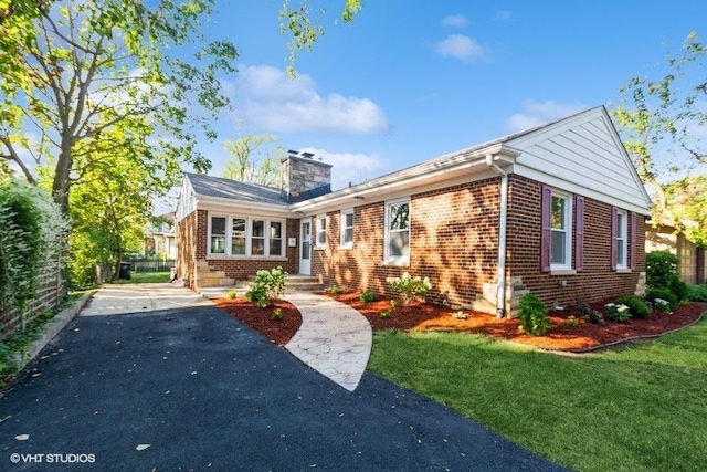 view of front of house with aphalt driveway, entry steps, a front yard, brick siding, and a chimney