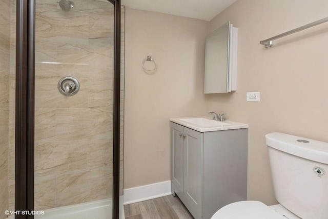 bathroom featuring a tile shower, toilet, vanity, wood finished floors, and baseboards