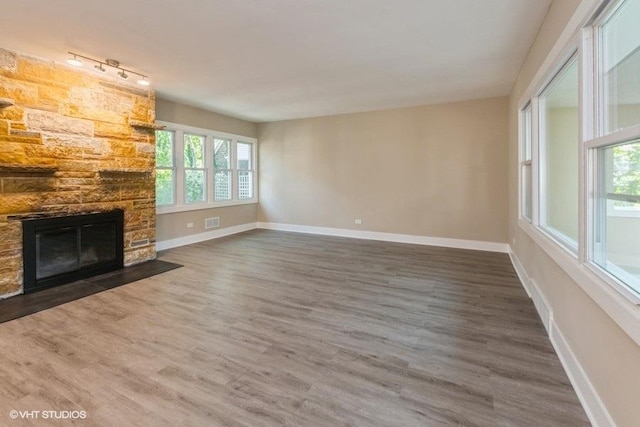 unfurnished living room featuring baseboards, wood finished floors, a healthy amount of sunlight, and a stone fireplace