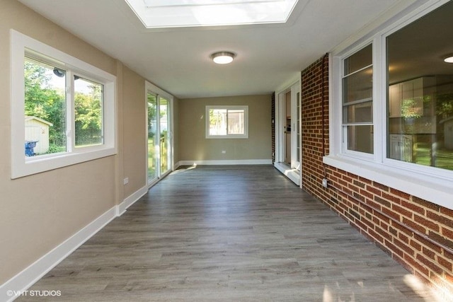 unfurnished sunroom with baseboards, wood finished floors, and brick wall