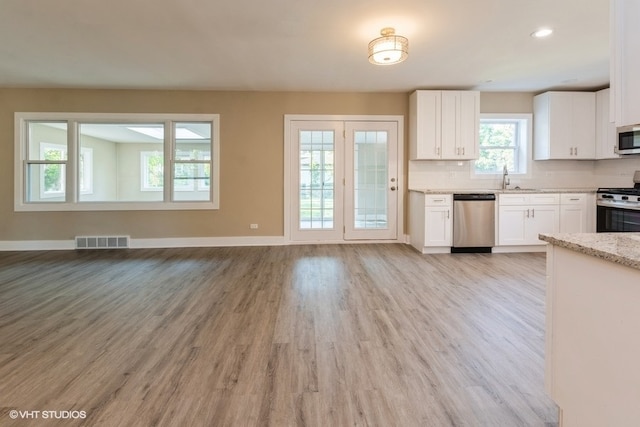 kitchen with light stone counters, white cabinets, sink, stainless steel appliances, and light hardwood / wood-style floors