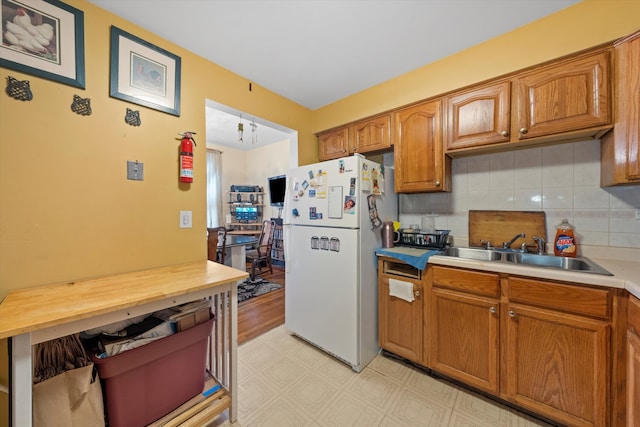 kitchen with light wood-type flooring, tasteful backsplash, sink, and white fridge