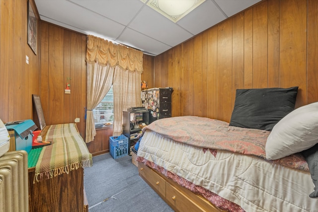 carpeted bedroom with a paneled ceiling and wood walls