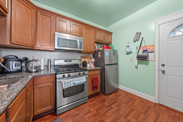 kitchen featuring appliances with stainless steel finishes, backsplash, dark stone countertops, and dark hardwood / wood-style floors