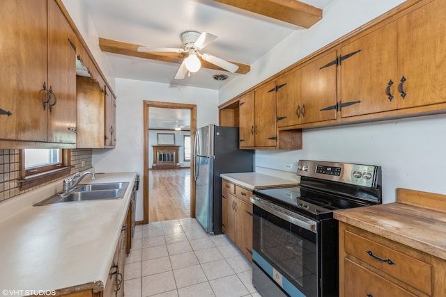 kitchen featuring ceiling fan, beamed ceiling, sink, stainless steel appliances, and light wood-type flooring