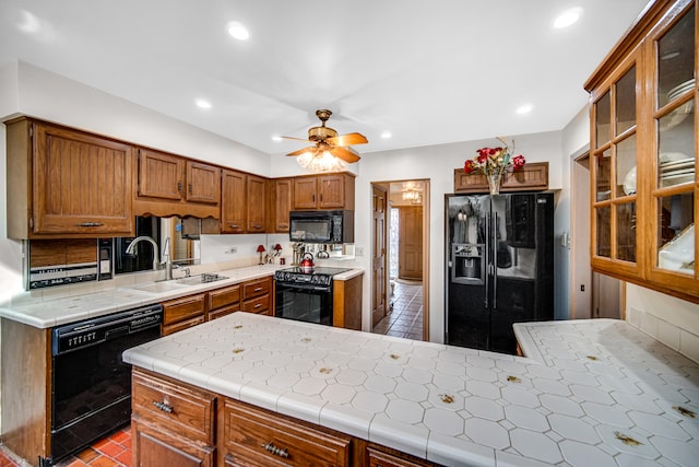 kitchen with tile counters, kitchen peninsula, sink, black appliances, and ceiling fan