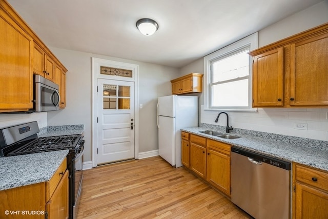 kitchen with appliances with stainless steel finishes, sink, light hardwood / wood-style flooring, and light stone counters