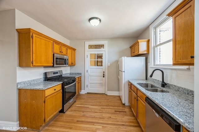 kitchen with stainless steel appliances, light stone counters, light hardwood / wood-style floors, and sink