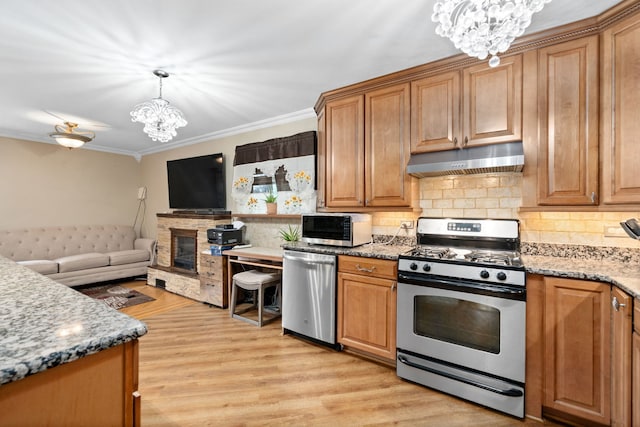 kitchen featuring appliances with stainless steel finishes, light hardwood / wood-style floors, a stone fireplace, crown molding, and a notable chandelier