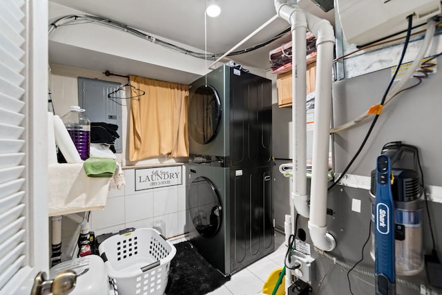 laundry area featuring electric panel, tile walls, stacked washer / drying machine, and light tile patterned flooring