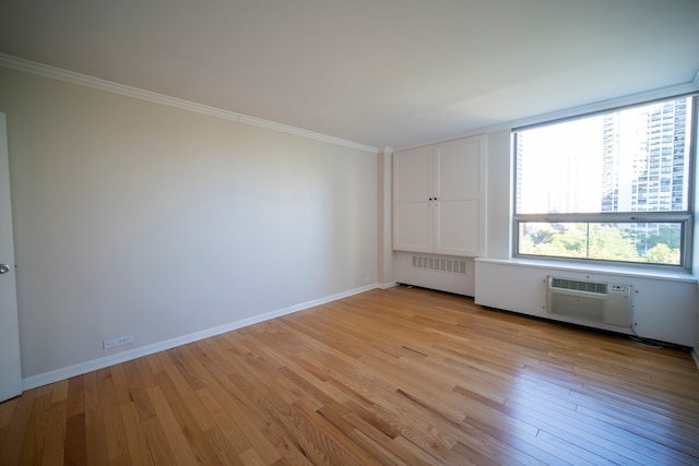 spare room featuring radiator, light wood-type flooring, ornamental molding, and a wall unit AC