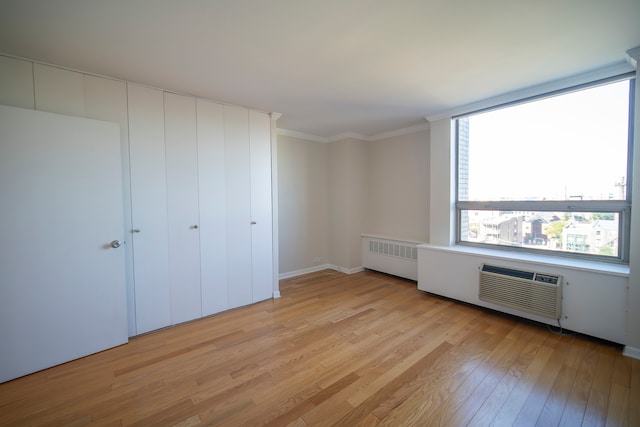 unfurnished bedroom featuring radiator heating unit, light wood-type flooring, ornamental molding, and a wall mounted AC