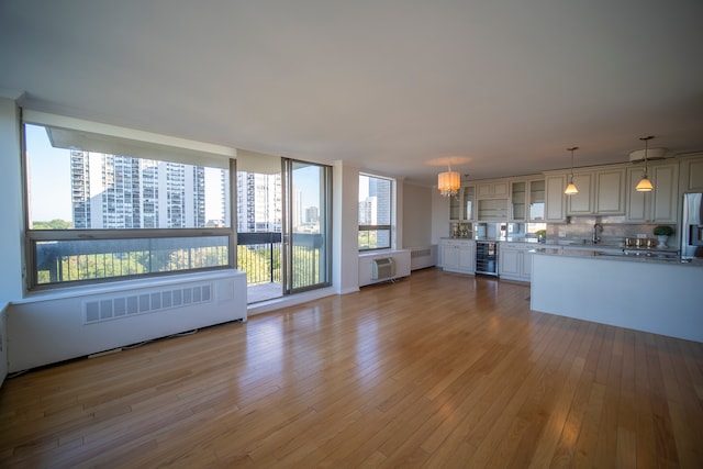 unfurnished living room featuring radiator heating unit, light wood-type flooring, wine cooler, and a wall mounted AC