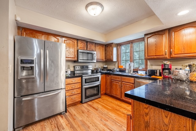 kitchen with sink, a textured ceiling, appliances with stainless steel finishes, a tray ceiling, and light wood-type flooring