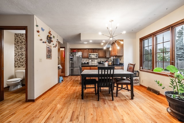 dining area with an inviting chandelier, light hardwood / wood-style flooring, and a textured ceiling