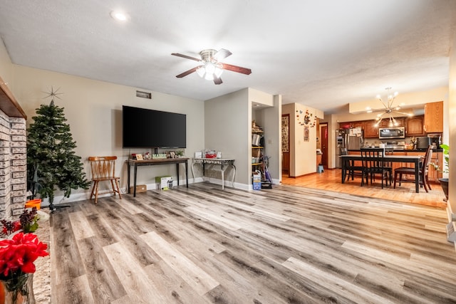 living room with ceiling fan with notable chandelier, light wood-type flooring, and a textured ceiling