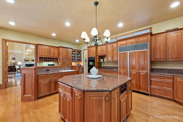 kitchen featuring light hardwood / wood-style flooring, decorative light fixtures, paneled built in refrigerator, a center island, and a notable chandelier