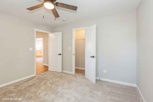 unfurnished bedroom featuring ceiling fan, light colored carpet, a closet, and a spacious closet