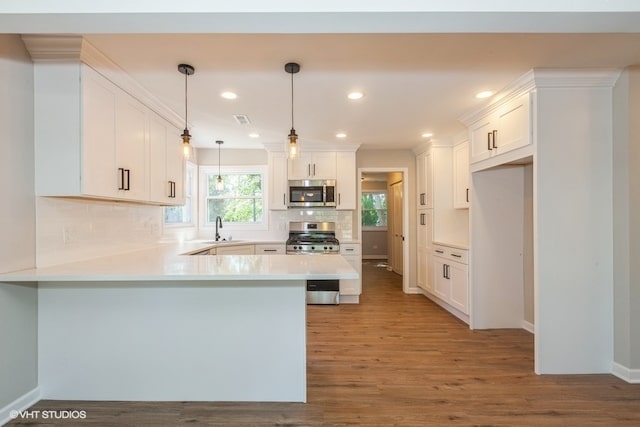 kitchen featuring white cabinets, kitchen peninsula, stainless steel appliances, hardwood / wood-style floors, and decorative light fixtures