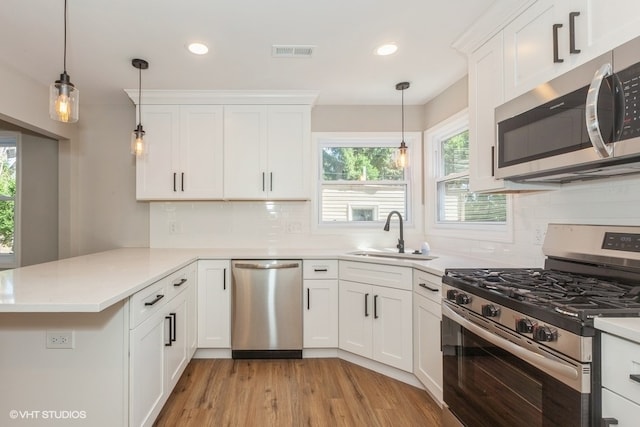 kitchen with white cabinetry, kitchen peninsula, stainless steel appliances, decorative light fixtures, and sink