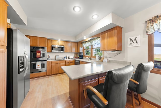 kitchen with light wood-style flooring, a sink, stainless steel appliances, a peninsula, and light countertops