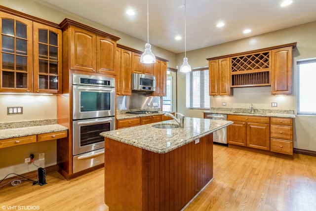 kitchen with light stone counters, sink, light hardwood / wood-style flooring, a center island with sink, and appliances with stainless steel finishes