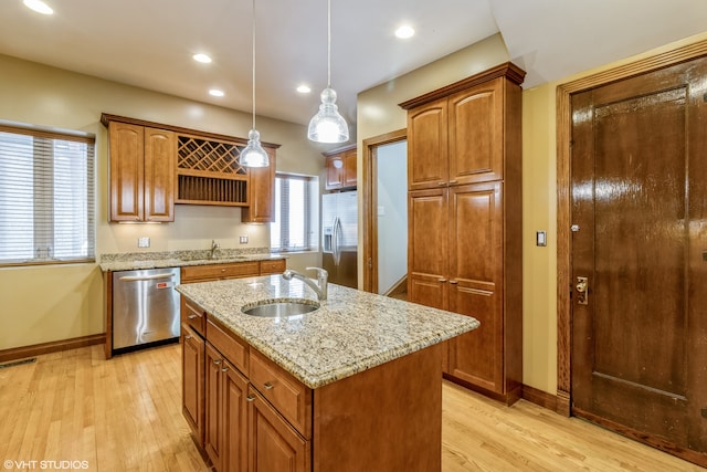 kitchen with appliances with stainless steel finishes, light hardwood / wood-style floors, decorative light fixtures, a kitchen island with sink, and sink