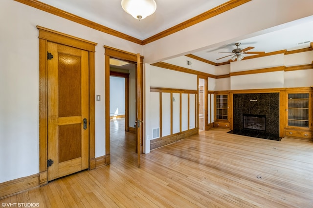 unfurnished living room featuring ceiling fan, ornamental molding, a premium fireplace, and light hardwood / wood-style floors