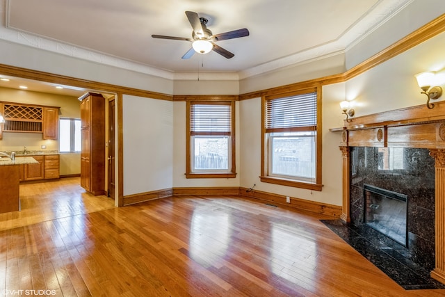 unfurnished living room featuring a healthy amount of sunlight, light hardwood / wood-style floors, ceiling fan, and a premium fireplace